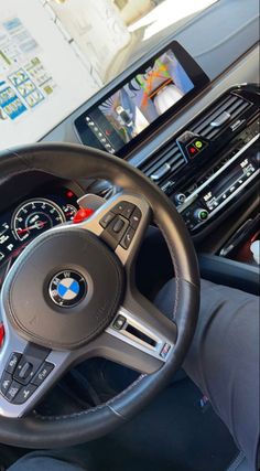 the steering wheel and dashboard of a car with an electronic display on the wall behind it