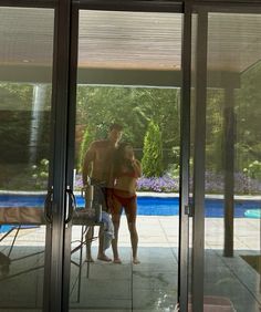 two people standing in front of a glass sliding door next to a swimming pool area