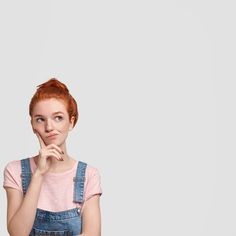 a woman with red hair and overalls is posing for the camera while holding her hand to her chin