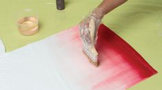 a person painting on a piece of paper with red and white paint next to a pair of scissors