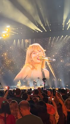 a woman singing into a microphone in front of a large screen with lights on it