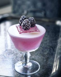 a dessert in a glass on top of a metal table with berries and ice cream