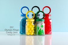 four glass jars with candy in them and olympic rings on the top one is filled with jelly beans