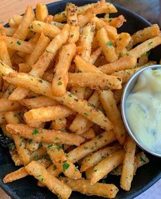 french fries with dip and parsley on top in a black plate, ready to be eaten