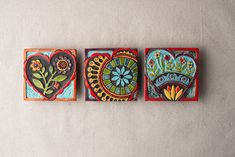 three hand painted tile pieces with flowers and hearts on them, all in different colors