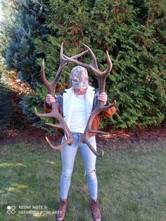 a woman standing in the grass holding two deer antlers