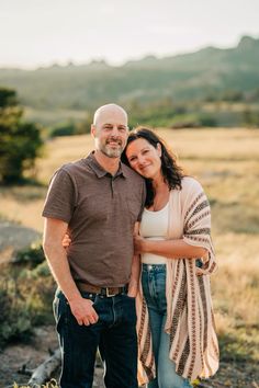 a man and woman standing next to each other in a field with mountains in the background