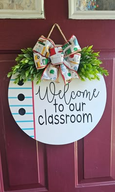 a welcome to our classroom sign hanging on the front door with green plants and bows