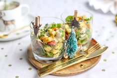 two glasses filled with food sitting on top of a wooden tray next to goldware