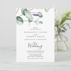 a white wedding card with greenery on it