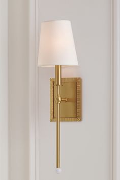 a wall light with a white shade on it's side and a door in the background