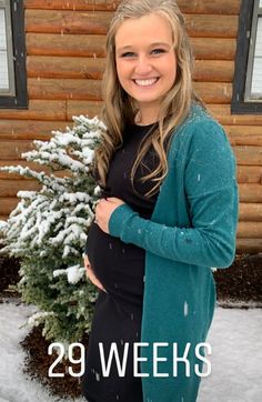 a pregnant woman standing in front of a snow covered tree with the text 29 weeks pregnant