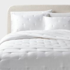 a bed with white linens and pillows on top of the headboard is shown