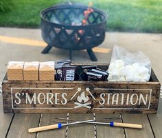 a wooden box filled with marshmallows on top of a table next to a fire pit