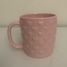 a pink mug with hearts on it sitting on a white counter top next to a wall