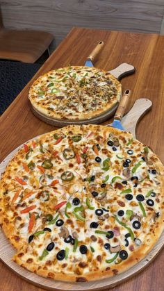 two large pizzas sitting on top of a wooden cutting board next to each other