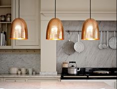 three lights hanging from the ceiling above a stove top oven in a kitchen with white cabinets and marble counter tops