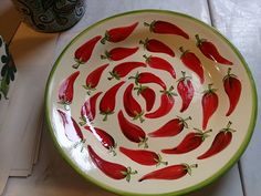 a bowl with red peppers painted on the side sitting on a table next to a vase