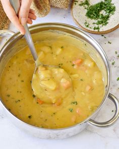 a person holding a spoon over a pot filled with soup and bread on the side