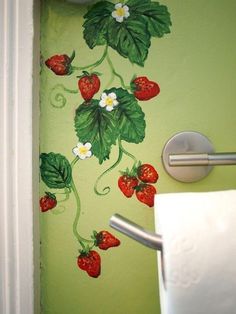 a green bathroom with strawberries painted on the wall and toilet paper dispenser