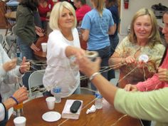 several women are gathered around a table with cups and plates on it while one woman is holding something in her hand