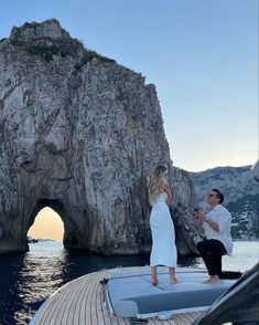 a man and woman standing on the bow of a boat in front of a rock formation