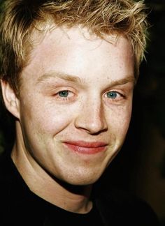 a close up of a person wearing a black shirt and smiling at the camera with blue eyes