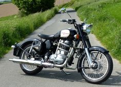 a black motorcycle parked on the side of a road next to green grass and trees