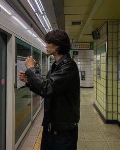 a man standing in front of a window next to a subway train platform with his hands clasped