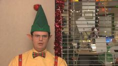 a man wearing a green elf hat and bow tie in front of a christmas tree