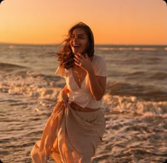 a woman standing on top of a sandy beach next to the ocean with her hands in her mouth