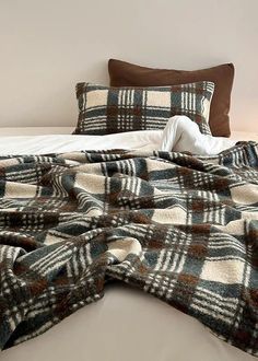 an unmade bed with plaid blankets and pillows on top of it, next to a night stand