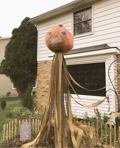 an orange pumpkin sitting on top of a wooden pole in front of a house with halloween decorations around it