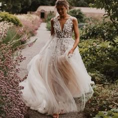 a woman in a wedding dress is walking down a path surrounded by plants and flowers