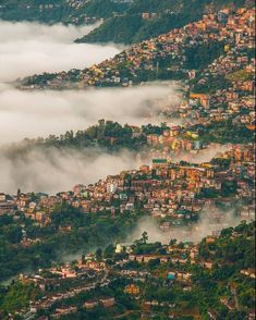 an aerial view of a city surrounded by fog and low lying clouds in the mountains