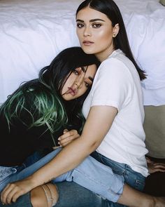 two women sitting on top of each other in front of a bed