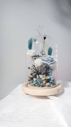 a glass dome with flowers and plants inside on a tablecloth covered surface in front of a white wall