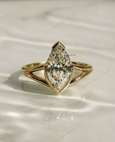 a yellow gold ring with a pear shaped diamond in the center on a white surface