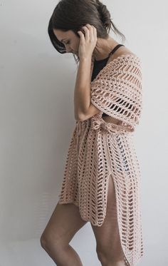 a woman standing in front of a white wall talking on a cell phone while wearing a crocheted shawl