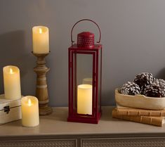 three lit candles sitting on top of a table next to books and a bowl with pine cones