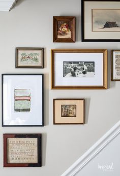 many framed pictures hang on the wall above a stair case in a home with white walls