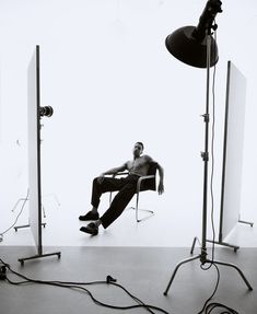 a black and white photo of a shirtless man sitting on a chair in front of three lights