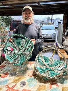 a man holding two baskets on top of a table next to other items in front of him