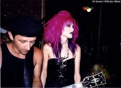 a woman with pink hair playing an electric guitar next to a man in black shirt