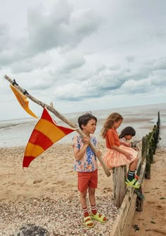 two young children are playing on the beach with an orange and yellow flag in front of them