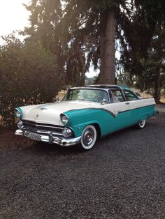 an old blue and white car parked next to a tree