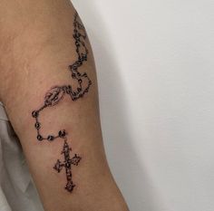 a tattoo on the arm of a person with a cross and rosary in black ink