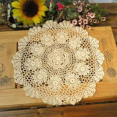 a doily is sitting on top of a wooden table next to a sunflower