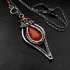 a red stone is hanging from a silver chain on a black surface with an intricate design