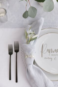 a place setting with silverware, napkins and greenery on the table top